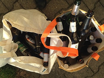 Aufsicht von zwei Stofftaschen, die nebeneinander stehen und mit leeren Glasbierflaschen gefüllt sind.