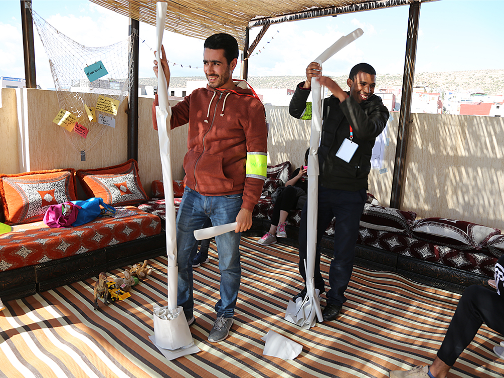 Zwei Teilnehmer halten die Papiertürme ihrer Gruppen mit stolzem Gesichtsausdruck fest.