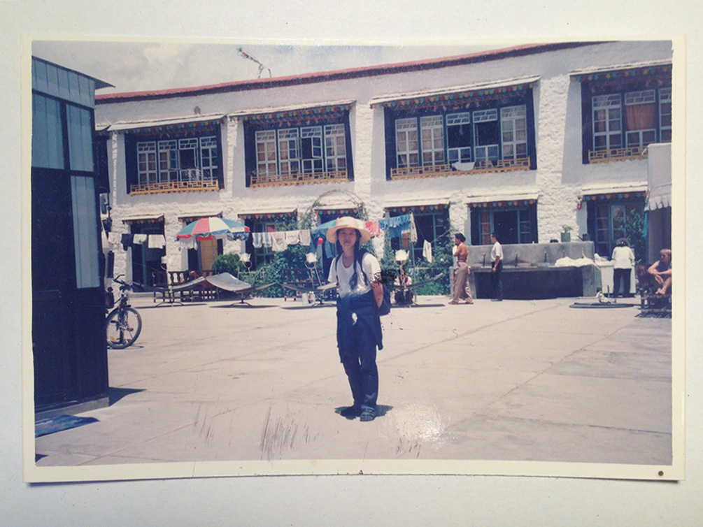 Ein altes, verblichenes Foto zeigt Shau Chung Shin, die im Hof eines Hostels in Lhasa, der Hauptstadt Tibets, steht. Die Sonne steht hoch, die Schatten sind klein. Sie trägt einen Strohhut, ein weißes T-Shirt und lange Zöpfe. Sie hat die Arme hinter ihrem Rücken verschränkt.