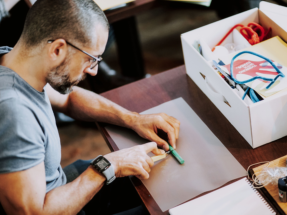 Ein Workshop-Teilnehmer schneidet mit einem Cutter grüne Knetmasse auf der Unterlage.